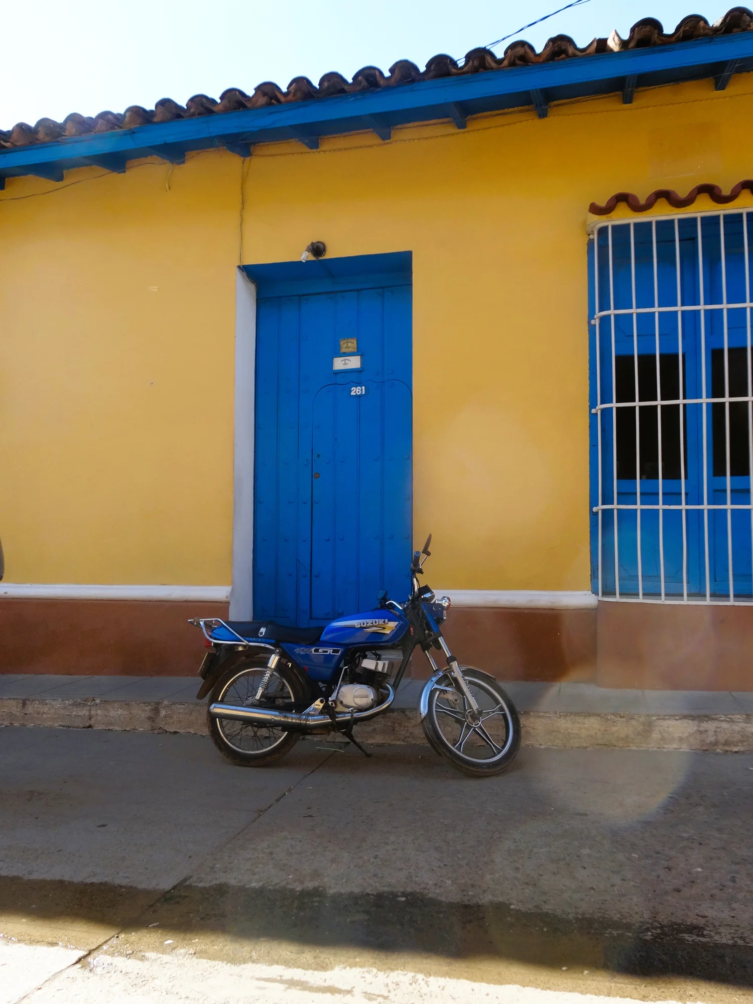 Moto Suzuki bleue stationnée devant une maison jaune aux portes, fenêtres et boiseries bleues — Bleu Sur Jaune