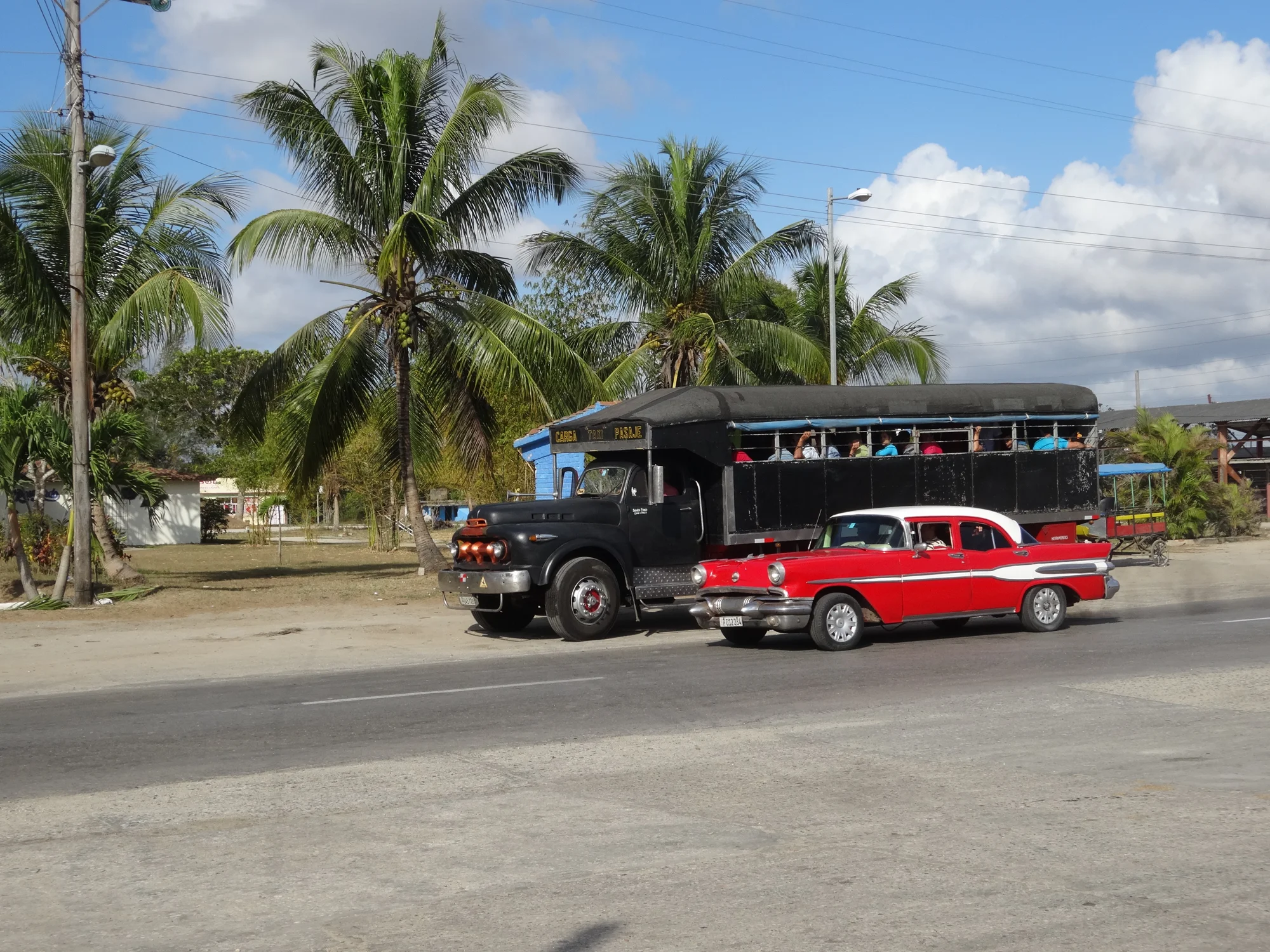 Voiture américaine rouge et blanche devant un camion noir transportant des passagers, Cuba — Chacun sa classe
