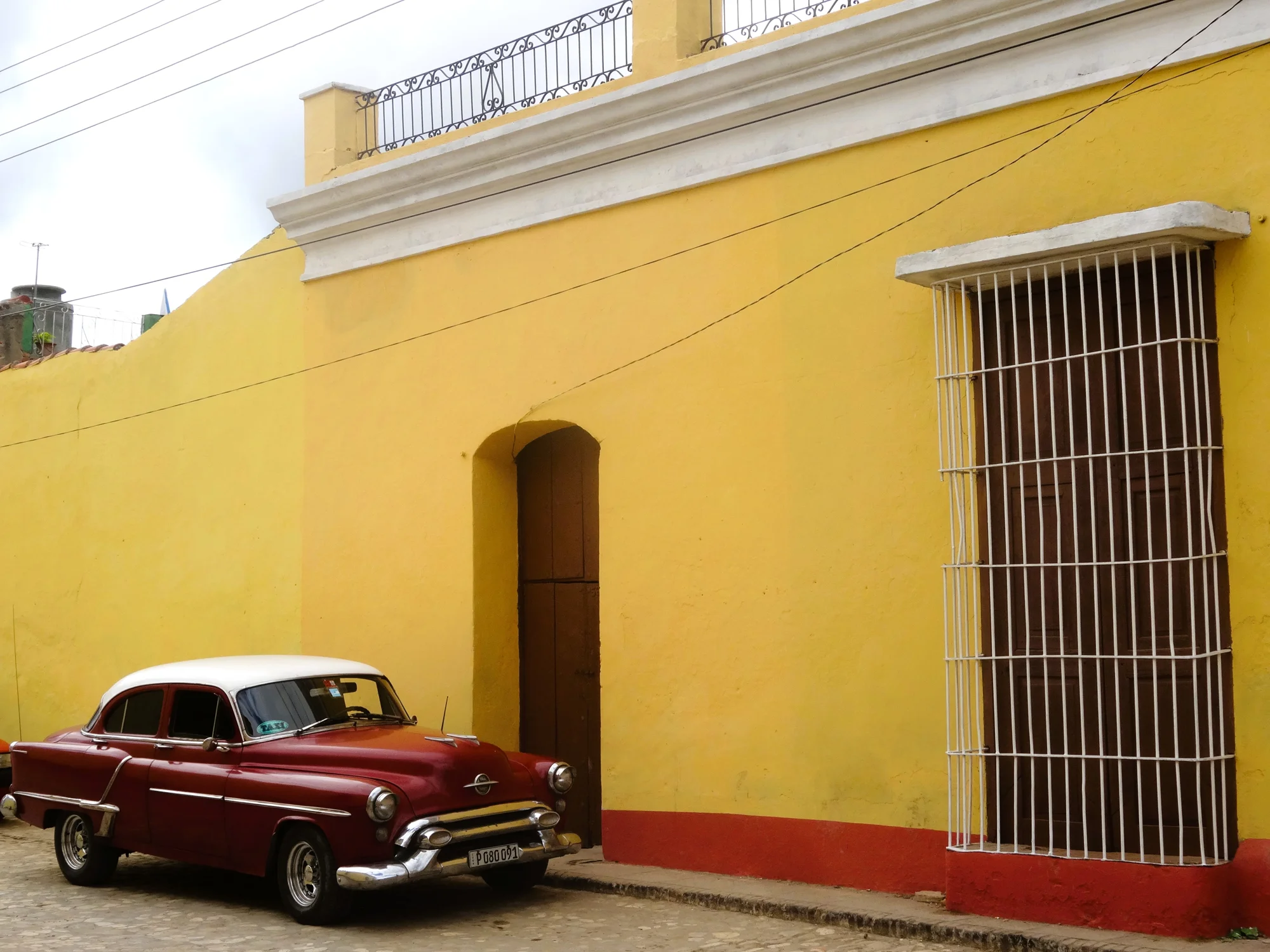 Voiture américaine ancienne rouge et blanche stationnée devant une façade jaune ocre à Cuba — Harmonie, Stéphane Pestel